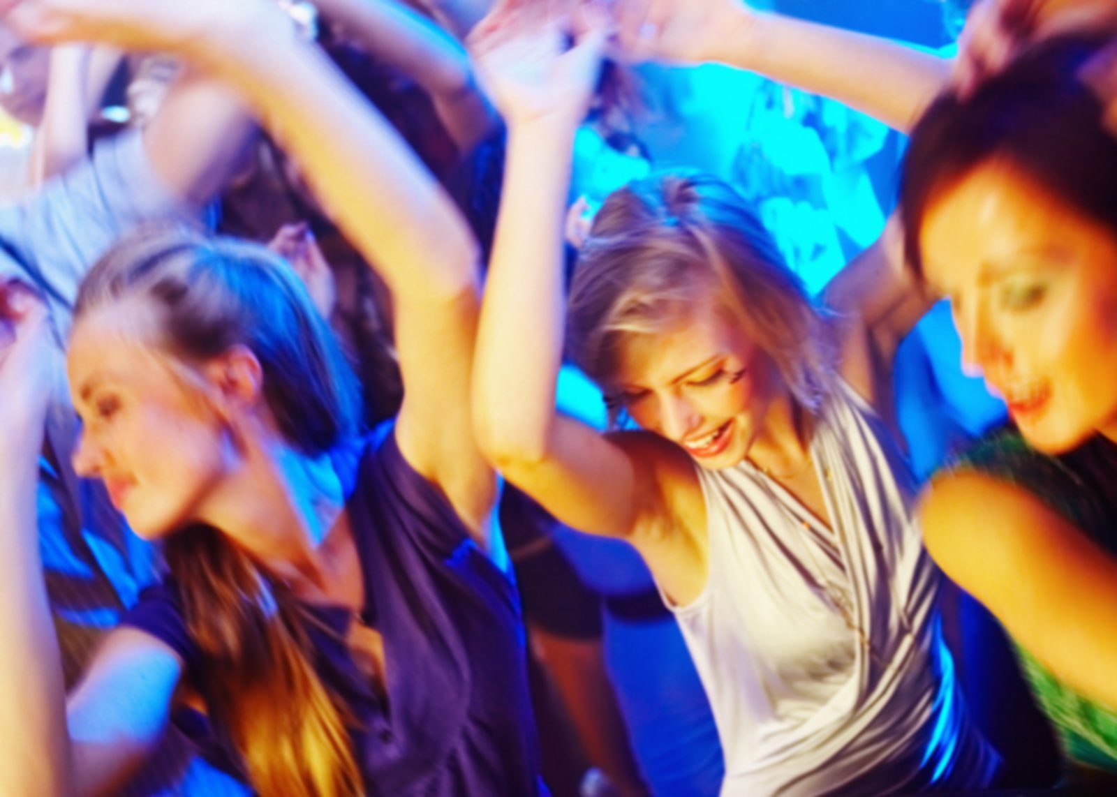 Dancers with arms raised on a club floor under blue and gold lights