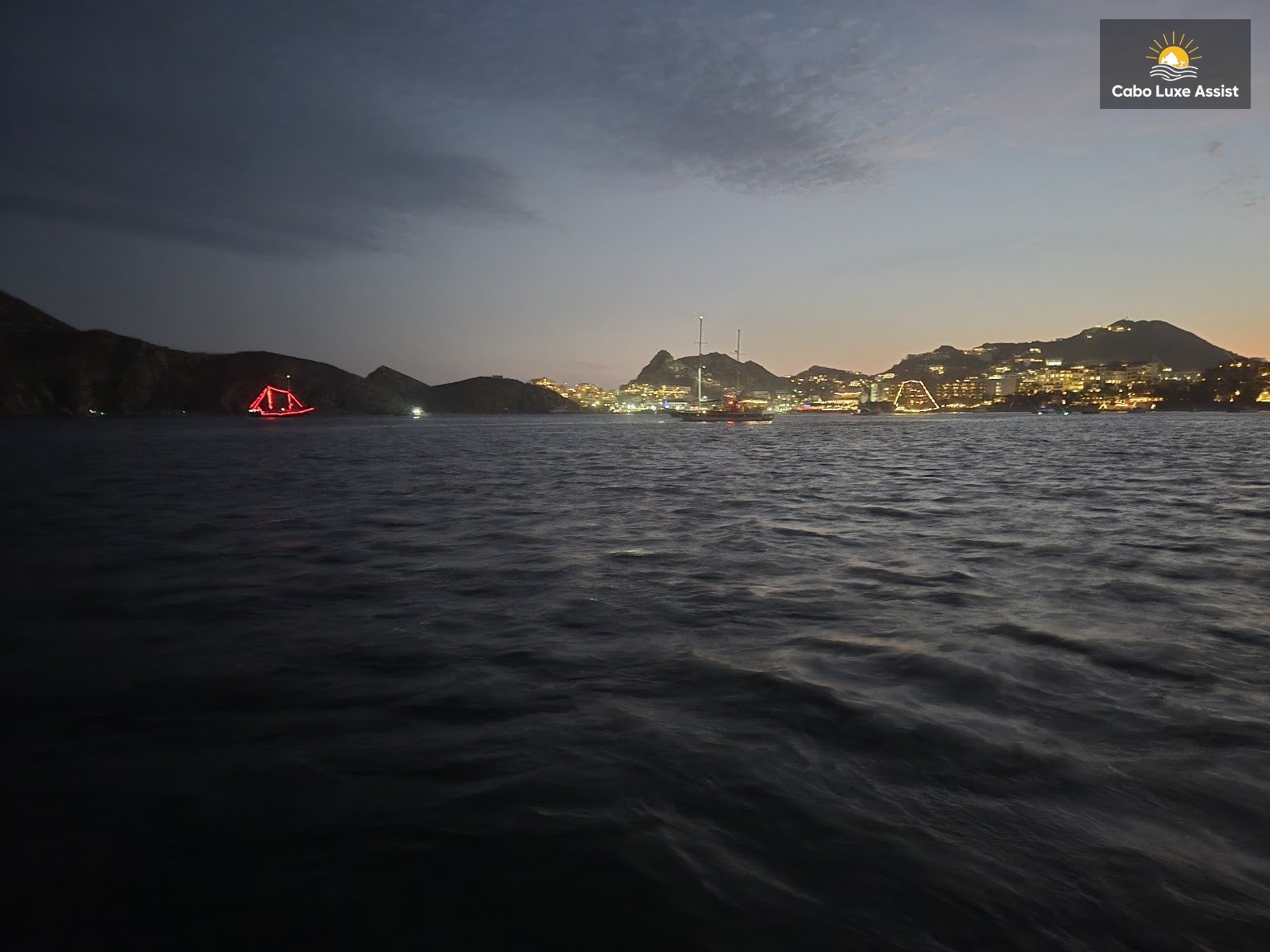 Cabo bay at dusk with boat lights and hillside resort glow